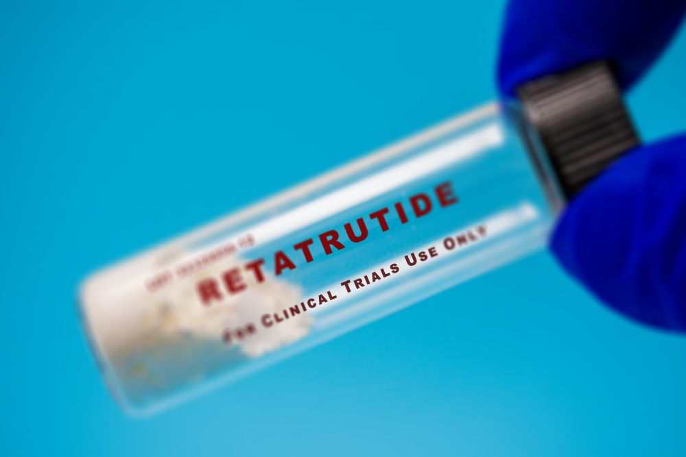 Retatrutide 1-gram vial with white powder for clinical trials use held by gloved hand on blue background