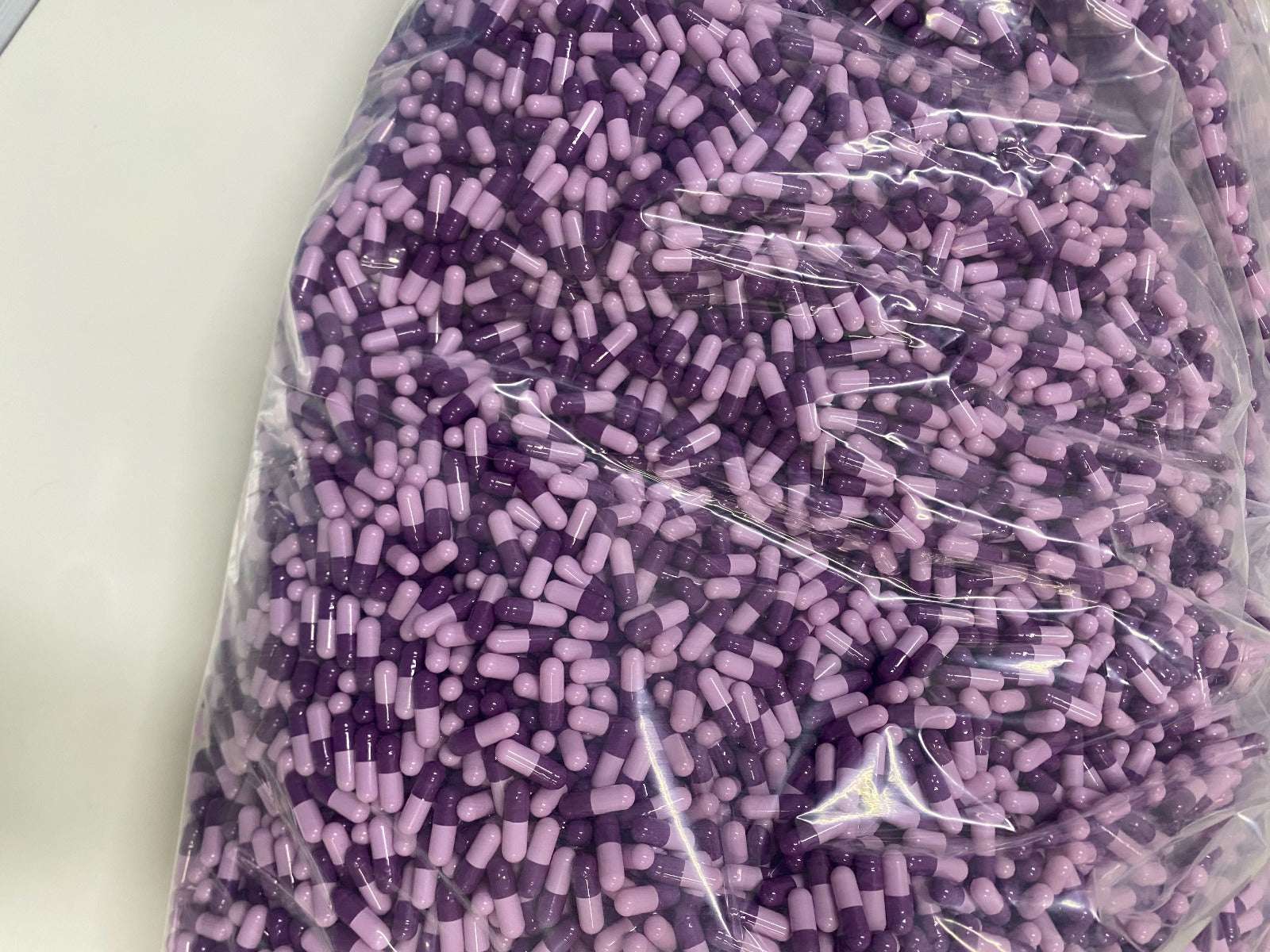 Bulk bag of purple and lavender Sermorelin 3mg capsules for pharmaceutical research and private labeling