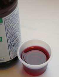 Herbal Cold-Flu Medicine syrup in a measuring cup and bottle for sinus and lung relief