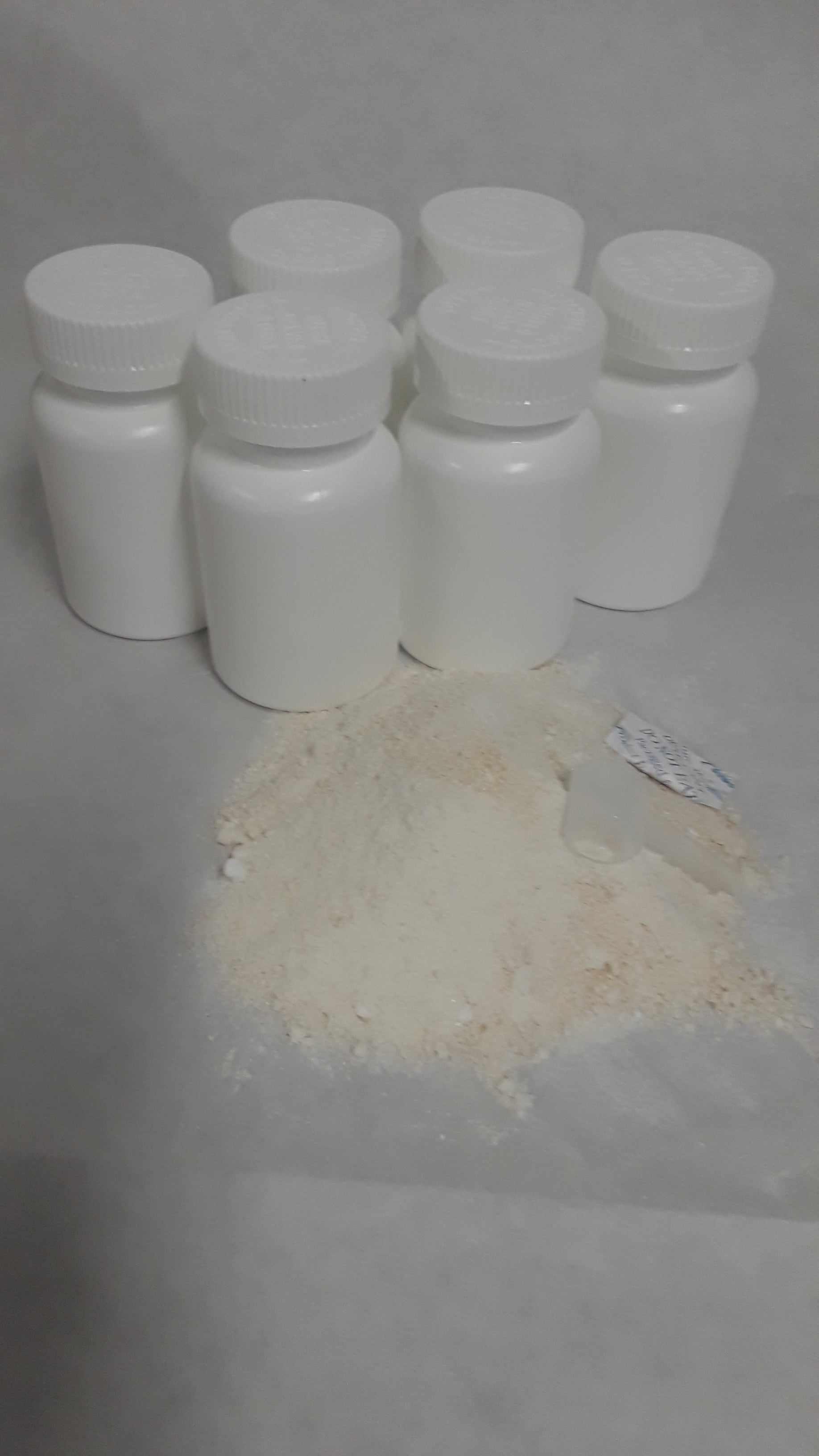 75 white bottles of skin lightening cosmetics ingredient with liposomal glutathione powder spilled on surface