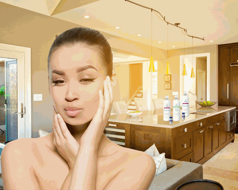Woman with clear skin touching face in bright kitchen with Glutathione Topical Liquid Gel bottles on counter